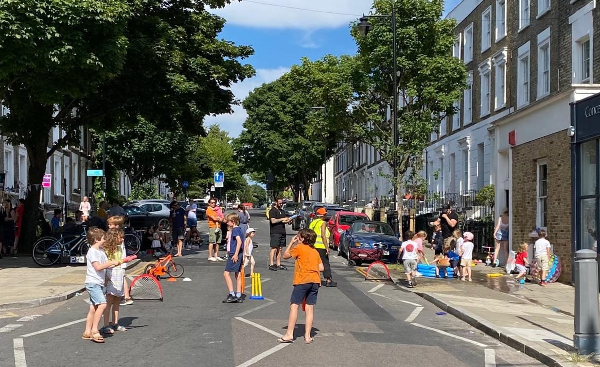 Adults and children play games in the middle of a road which is closed to motor traffic.